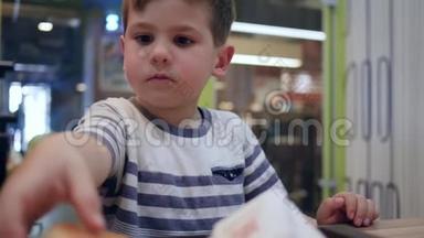 可爱的饥饿男孩在街头咖啡馆用有害的食物来消除饥饿，小男孩在餐桌上吃汉堡，胃口很好
